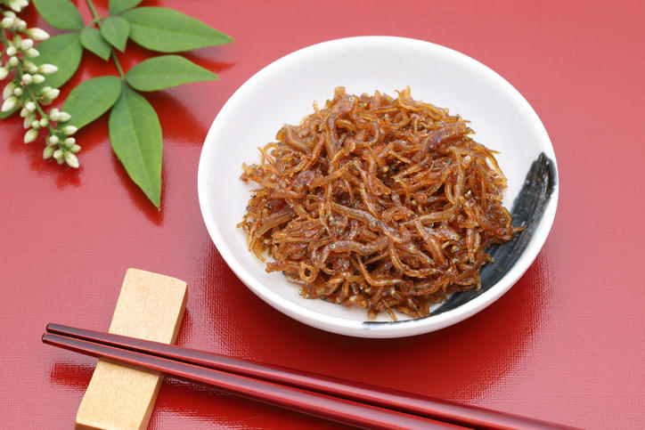 赤い背景に置かれた白い豆皿のなかのちりめんじゃこ