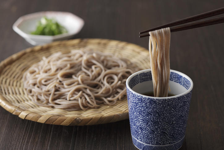 ザルに乗せられたそばを食べようと箸で掴んでいる