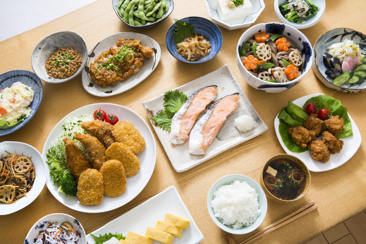 食卓の上に焼き鮭・コロッケ・玉子焼き・煮物などが並べられている様子