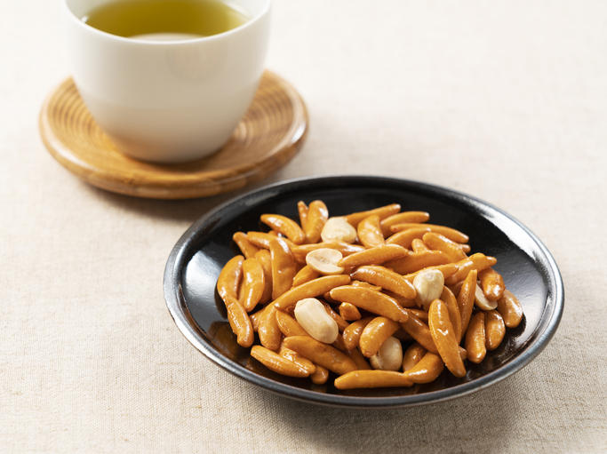 黒い丸皿に盛られた柿の種と白い湯呑みに入ったお茶
