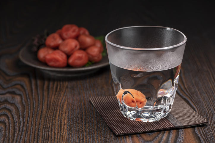 木製のテーブルに置かれた焼酎のお湯割りと皿に盛られた梅干し