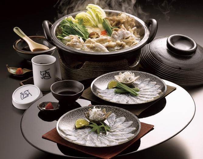 黒ベースの食器に盛り付けられ食卓に並ぶふぐ鍋、ふぐ刺し、ひれ酒