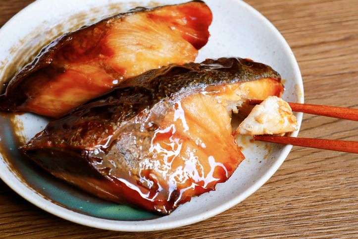 お皿にのったぶりの照り焼きを箸でつまむ様子