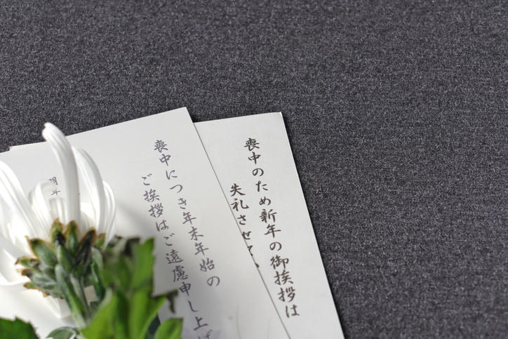 2枚の喪中はがき、白い仏花が置かれている