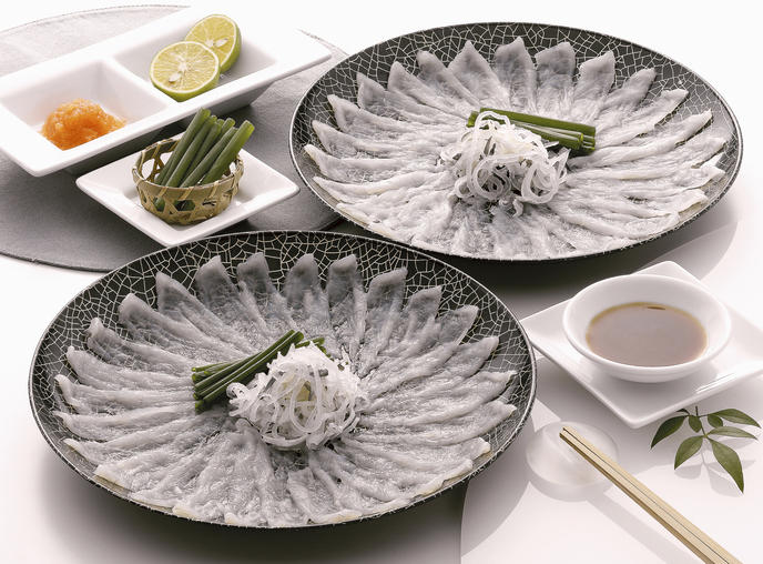 黒い皿に盛り付けられた2皿のふぐ刺しと小皿の薬味（もみじおろし・かぼす）と醤油
