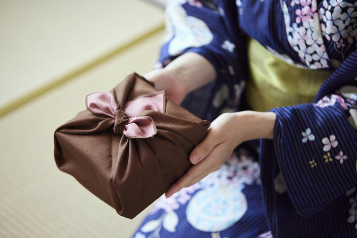 紺色の着物を着た方が畳の上で風呂敷包みを渡している