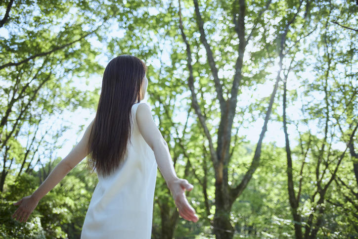 新緑の中で女性が手を広げて立っている