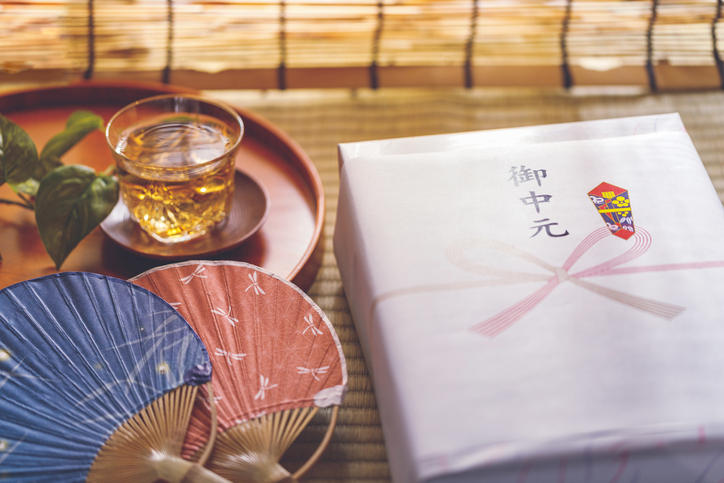 お中元の箱の横に、お盆にのった麦茶と、うちわ2枚が置かれている