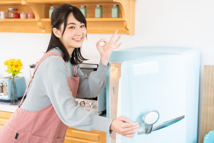 冷蔵庫を開けながらOKサインでほほ笑むエプロン姿の女性