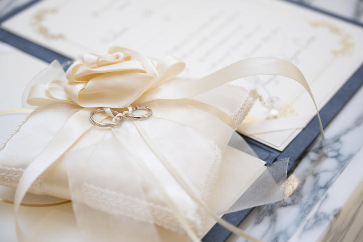 クリーム色のリボンがかかった白いクッションの上に結婚指輪がふたつ並んで置いてある写真