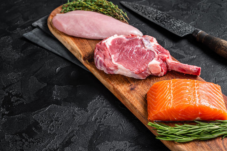 木製のプレートに置かれた生のサーモン、牛肉、鶏肉