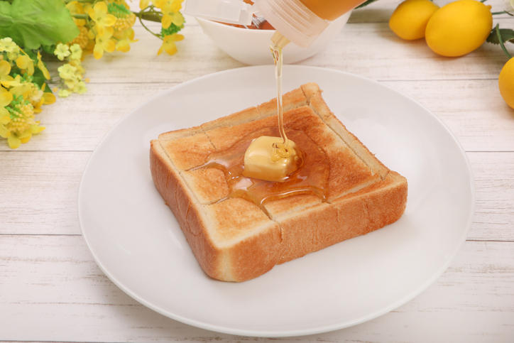 白い皿にのったバタートーストにはちみつをかけている様子