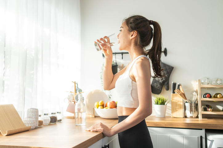窓辺でグラスに入った水を飲む健康的な女性