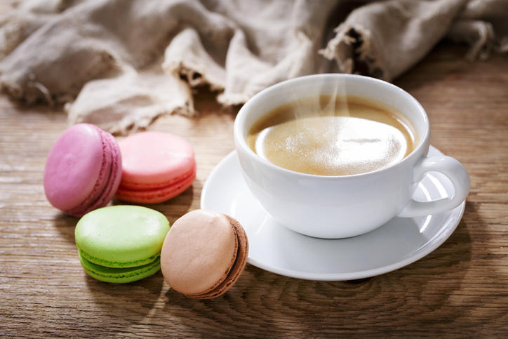 コーヒーが入ったカップの横に、4種類のカラフルなマカロンが置かれている