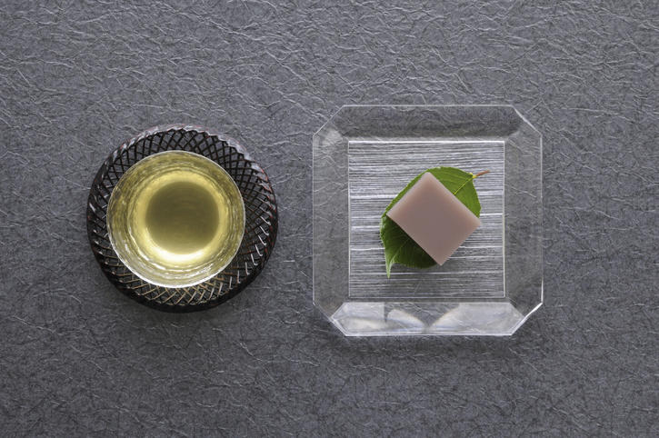 グレーの背景に置かれた日本茶と透明な皿の上の和菓子のトップアングル
