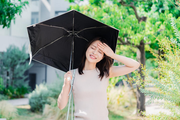 女性が緑の中を日傘をさして暑そうに歩いている