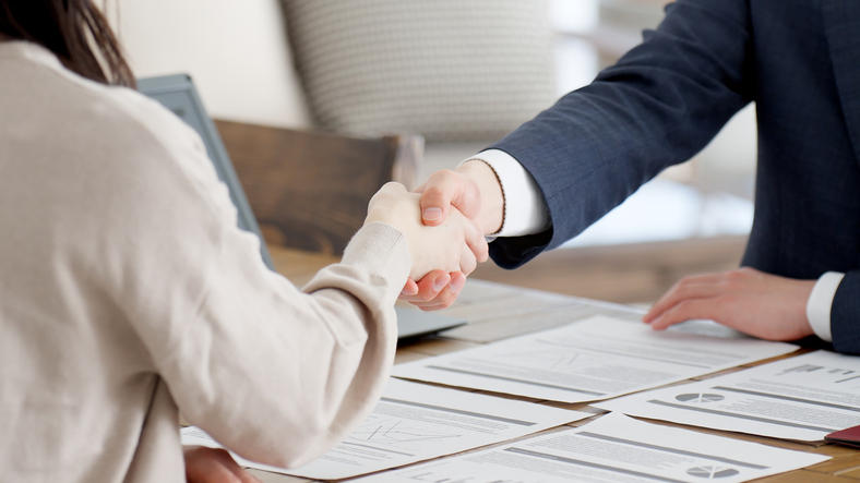 社会人同士がデスクの上で握手をしている
