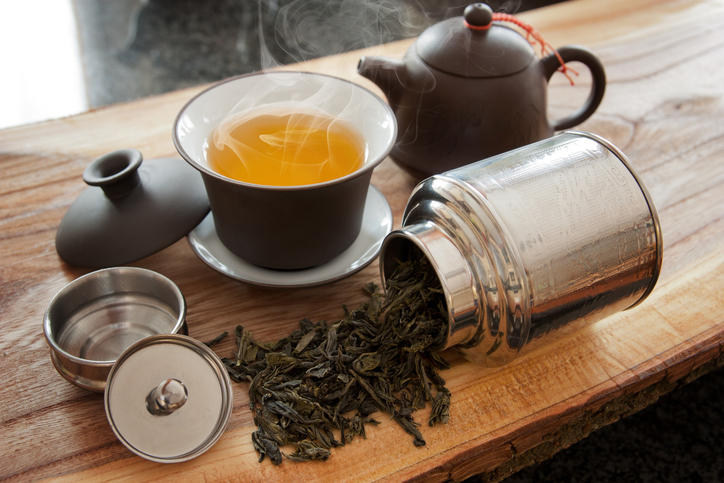 木のテーブルの上に烏龍茶が入った茶色い茶器が置かれ、その横には銀色の茶筒が寝かせた状態で置かれており、中から茶葉がこぼれている