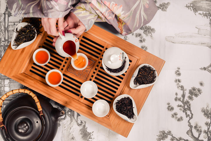 伝統的な中国茶の茶器や茶葉とお茶を茶碗に注ぐ女性の手