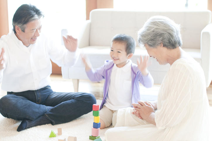 家で孫の赤ん坊を抱く祖父とそれを見ている祖母