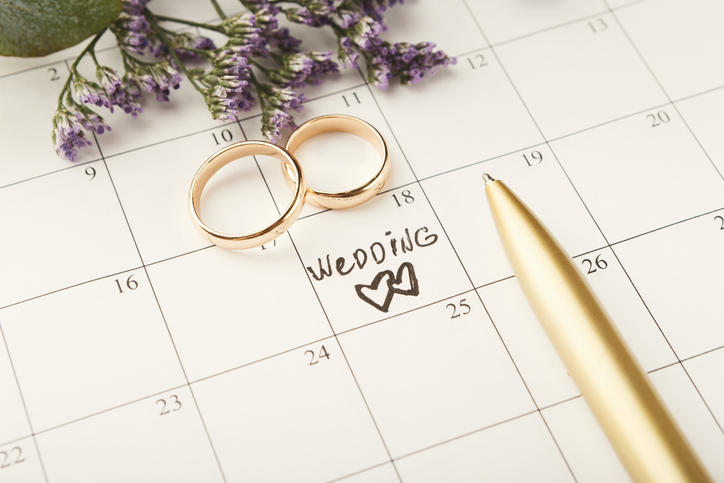 weddingの文字が記されたカレンダーの上にペンと2つの指輪が置かれている様子