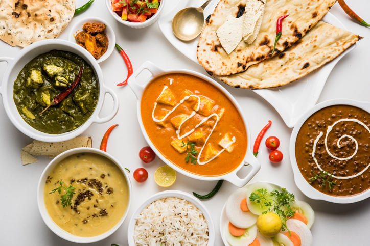 白い皿に盛られたバターチキンカレー、ひよこ豆カレー、グリーンカレー、キーマカレーとナン