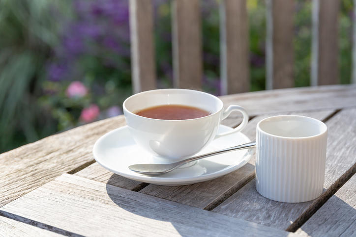 テラスにある木のテーブルに紅茶が注がれた白いティーカップが置かれている