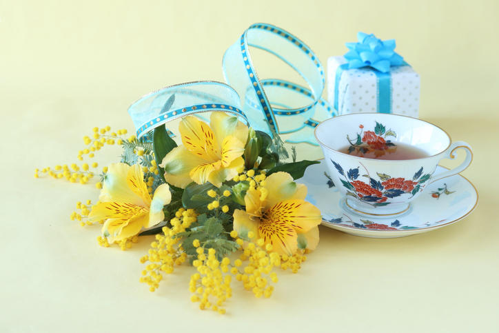 黄色い花束とブルーのギフトボックスと紅茶が注がれた花柄のティーカップが置かれている
