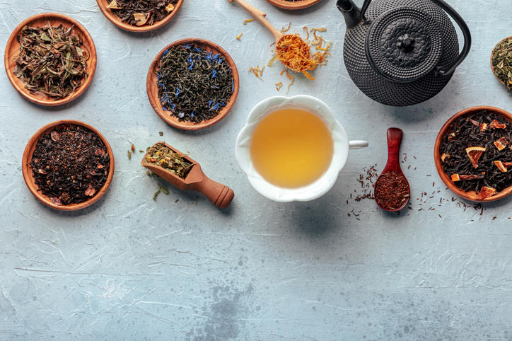 木の小皿に乗せられた紅茶、緑茶、白茶などの茶葉と白いカップに注がれたお茶と黒い鉄瓶が置かれている