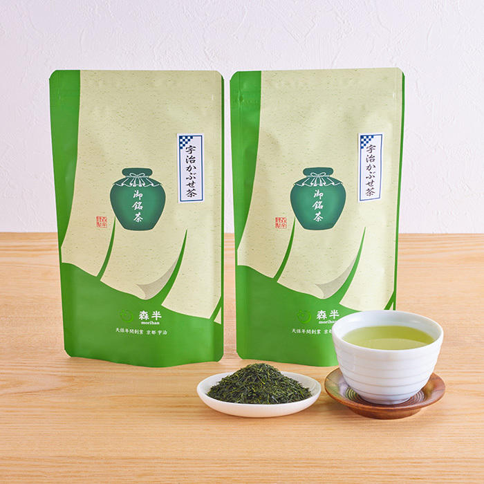 茶匠森半のかぶせ茶2袋と白い湯飲みに注がれた緑茶と茶葉が乗せられた白い小皿が置かれている