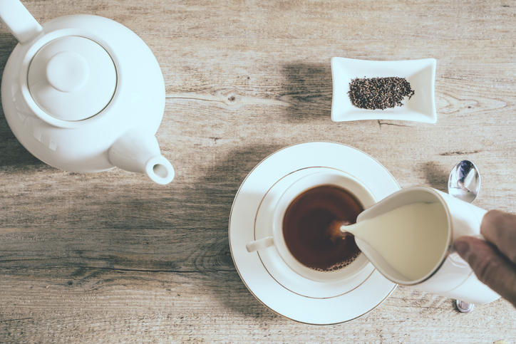 ティーポットと紅茶が入ったティーカップにミルクが注がれている