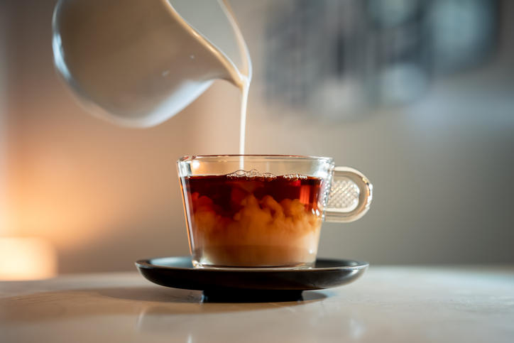 紅茶がはいったガラスのティーカップにミルクが注がれている