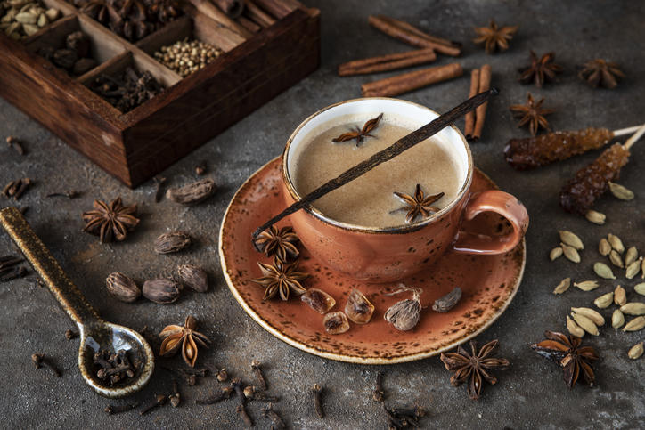茶色のカップに注がれたマサラチャイと、スパイスが入った木箱が置かれている
